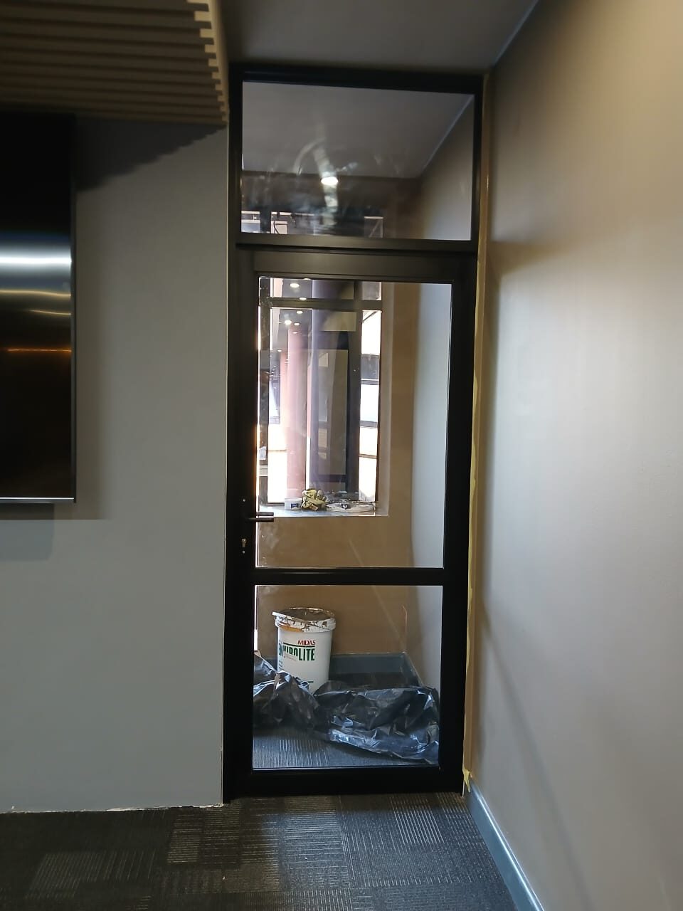 black aluminium interior door with a glazed fanlight in an office corridor