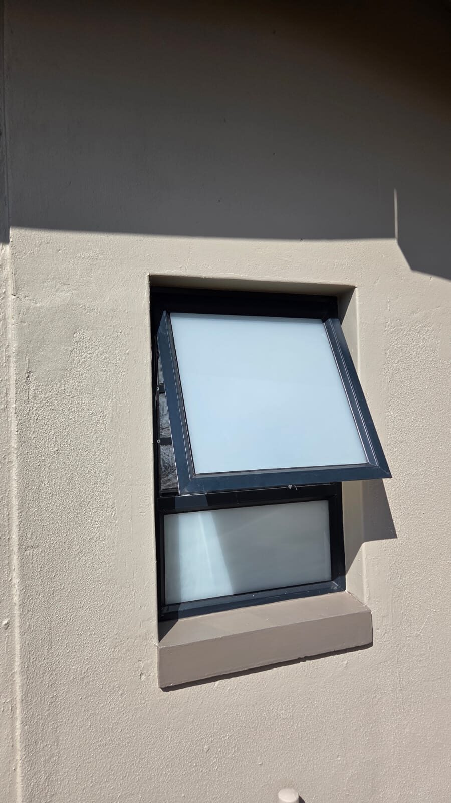 charcoal top-hung awning window with obscure glass on a plastered wall