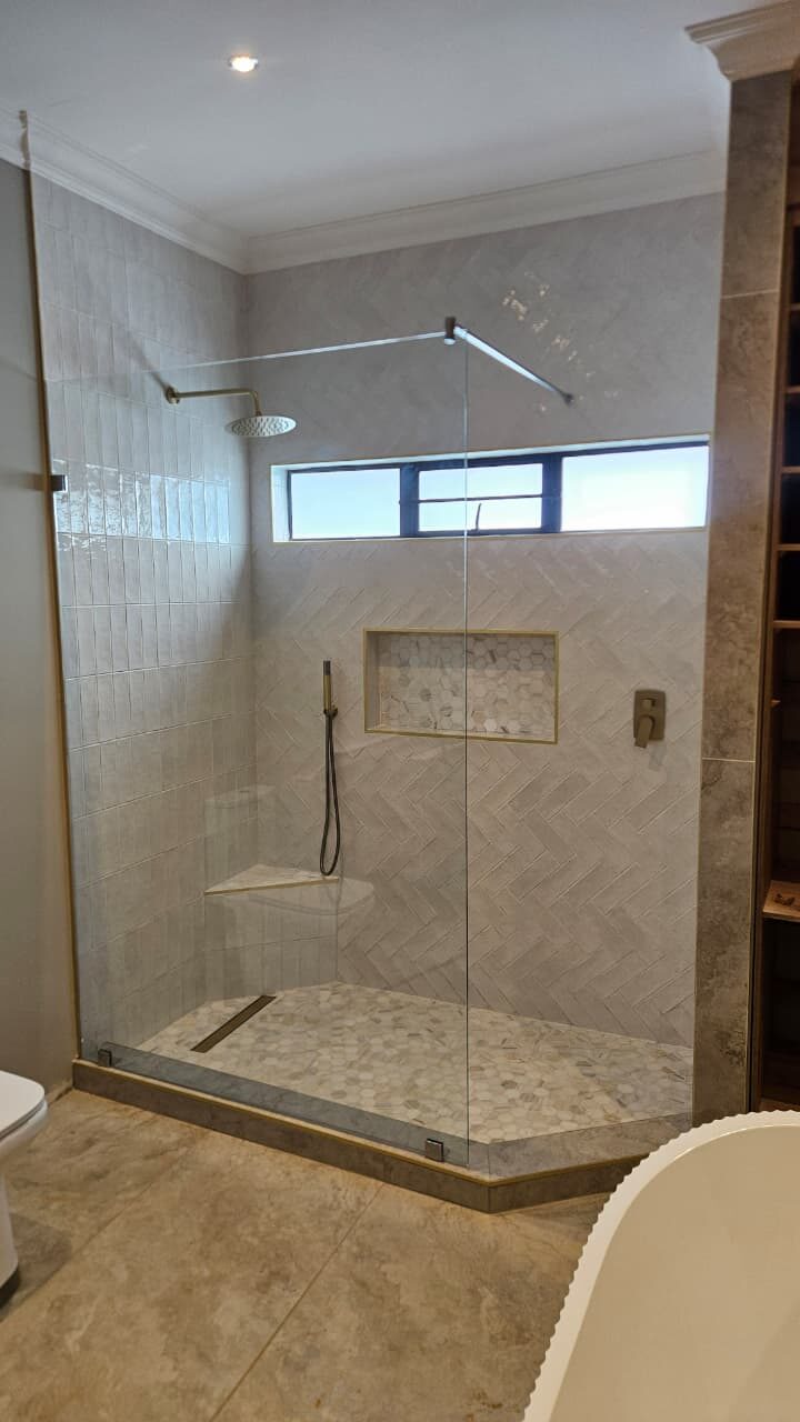 frameless glass shower screen with herringbone tiling and a brass support rail